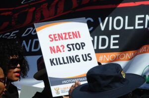 A poster in a protest that says "Senzeni Na? Stop Killing Us"