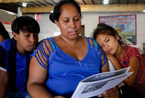 A woman reads a newspaper while two children look on