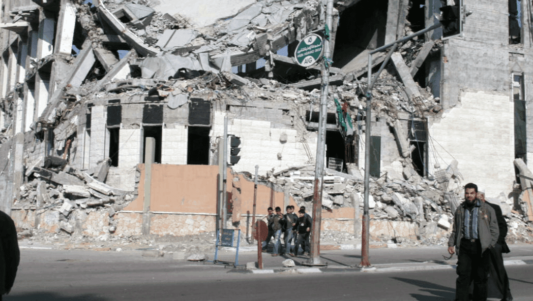 People walk in the street past a bombed building