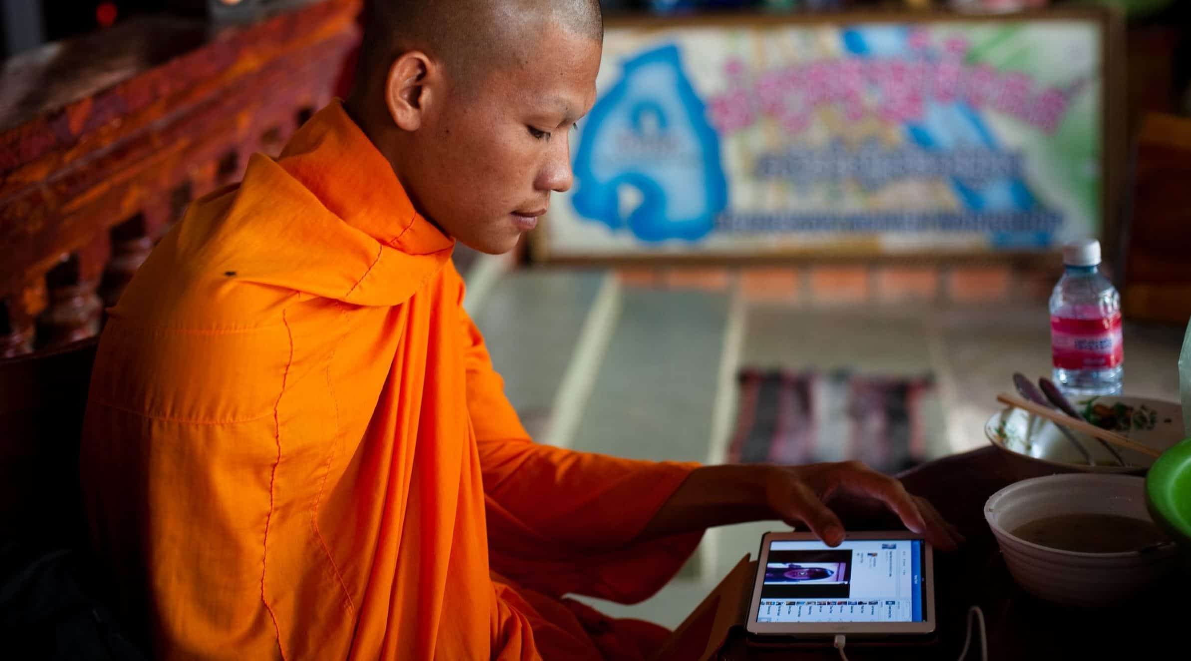 A man wearing an orange robe holds a tablet