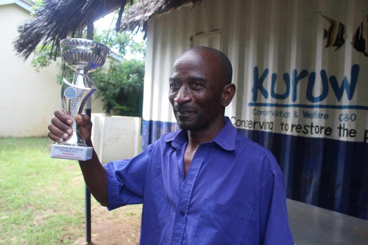 A man stands outside a metal building holding an award in his hand