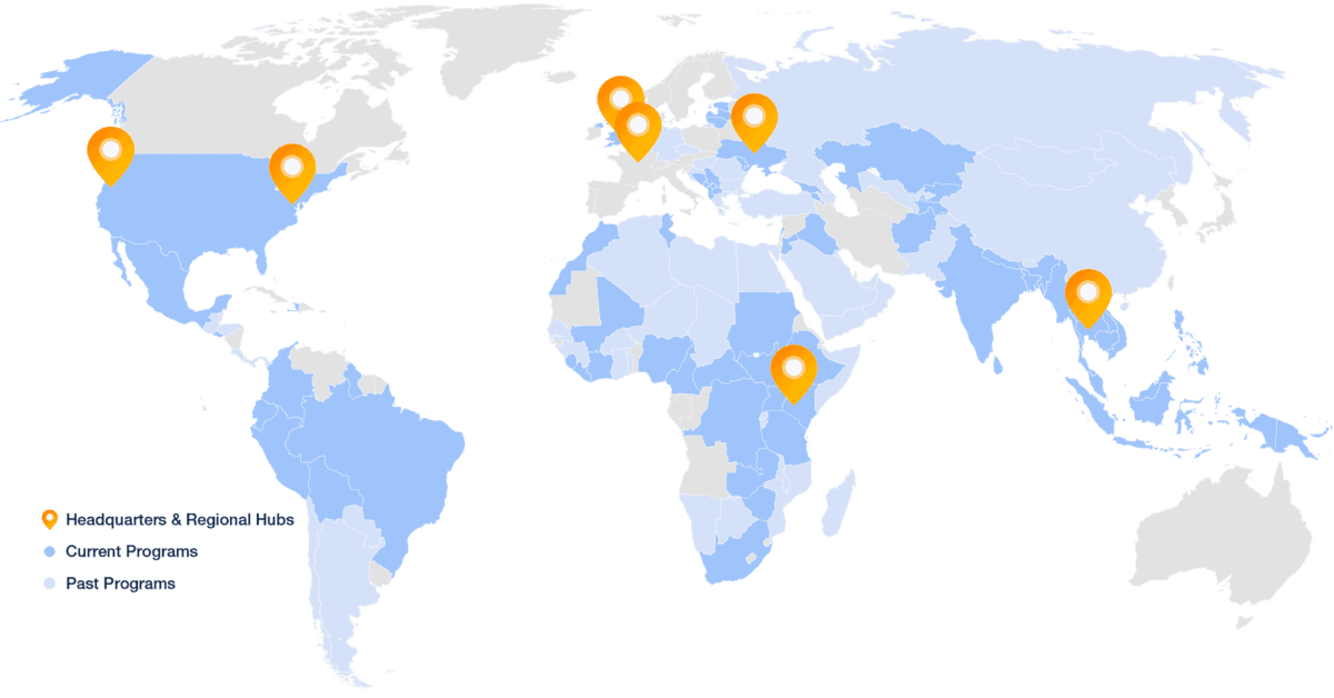 World Map with some countries colored medium blue (current programs), some light blue (past programs), and some gray (have never worked there). There are 7 orange markers showing location of headquarters and regional hubs
