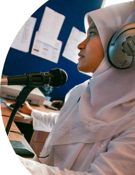 A woman wearing a head scarf and headphones sits in front of a mic