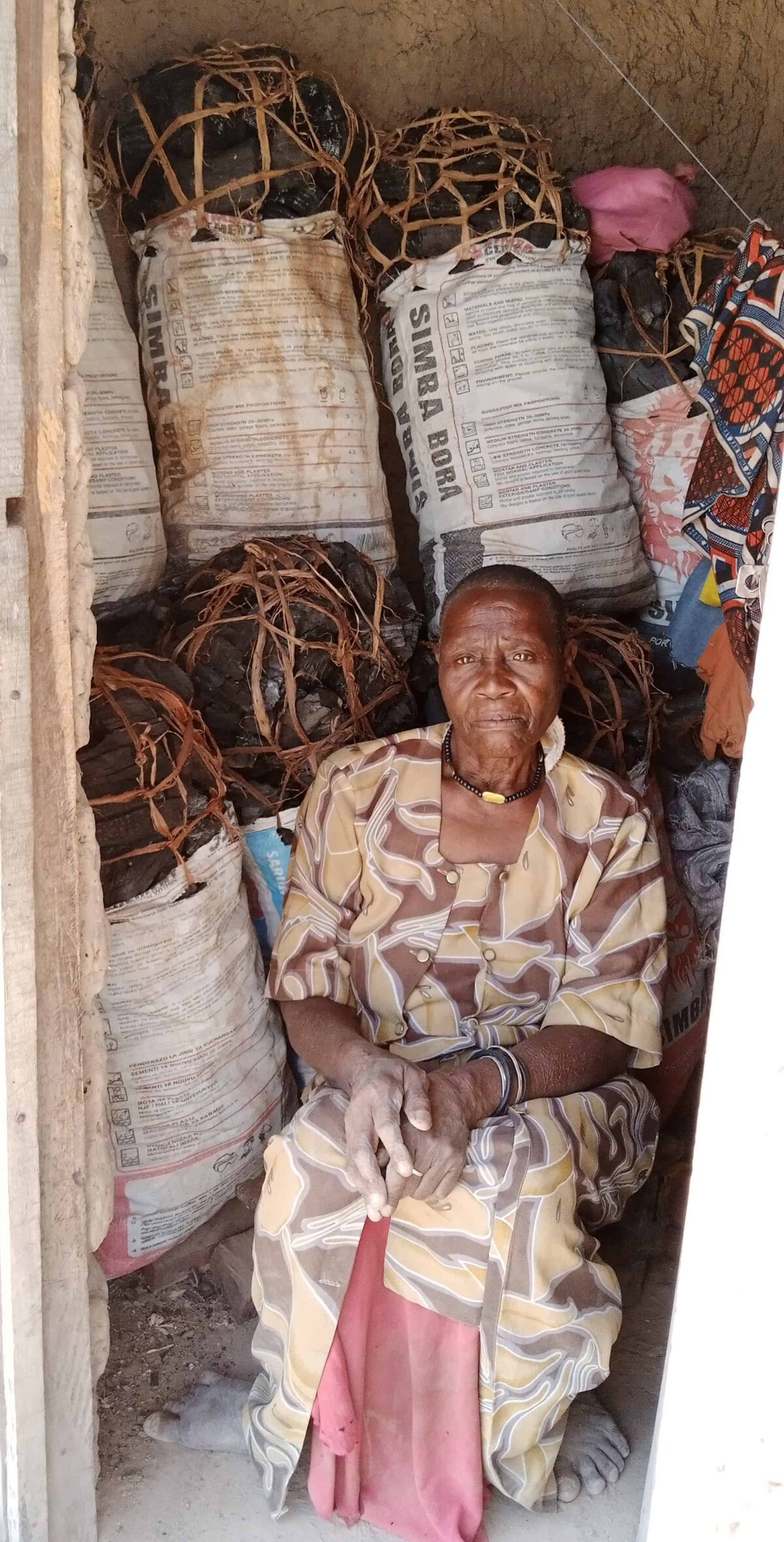 A woman wearing a print dress sits in front of a stack of large bags