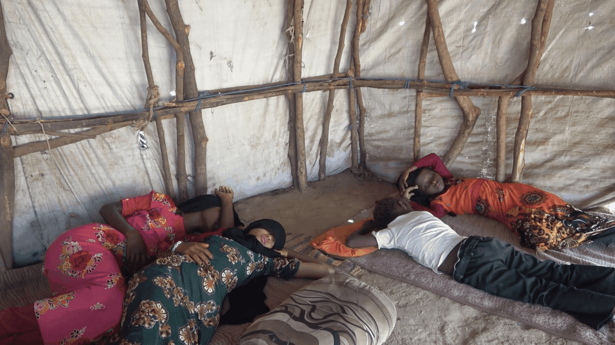 Children lie on mats on the floor of a tent