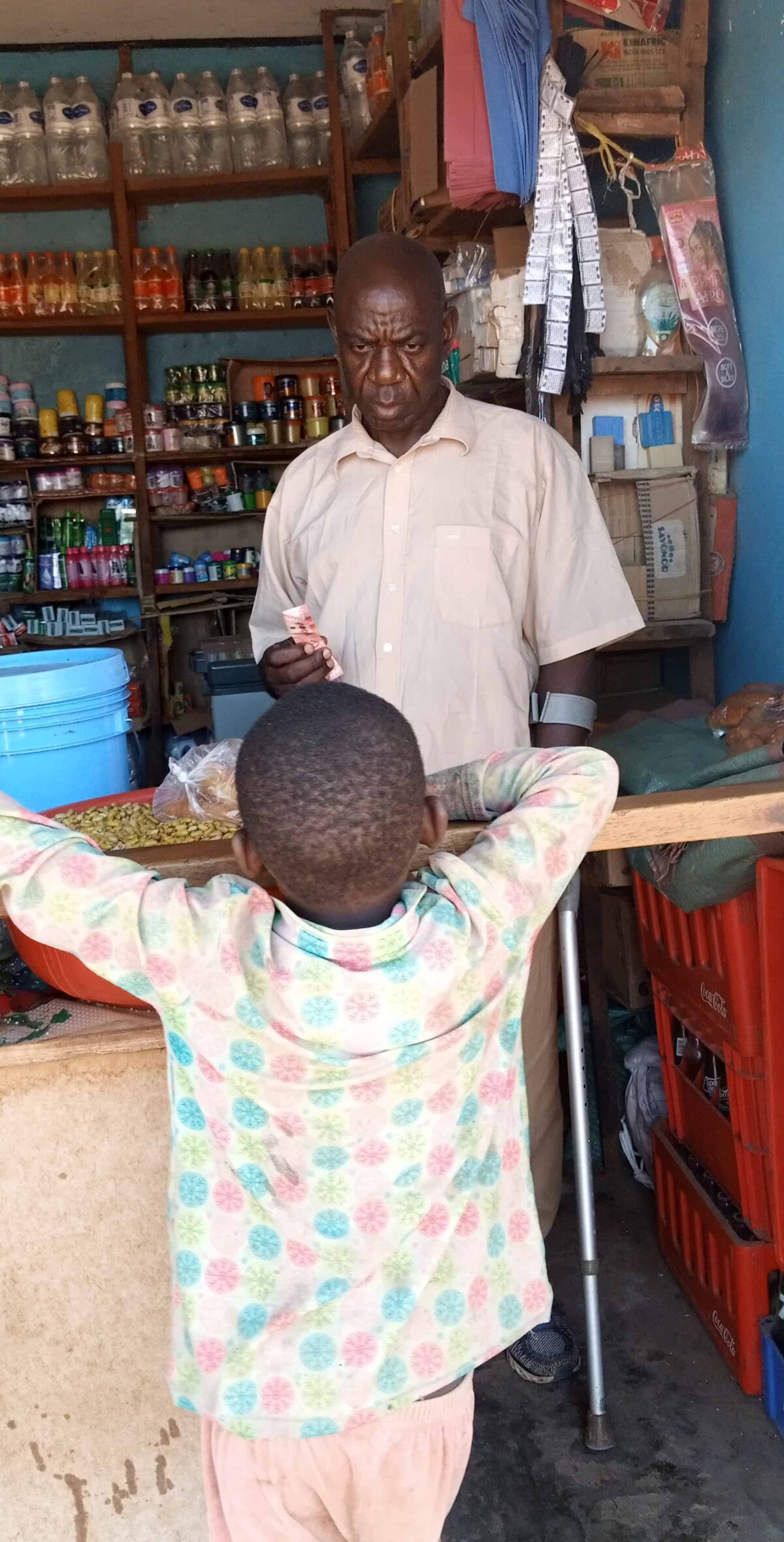 A man stands behind a counter in a store; a young boy looks over the counter on the other side.