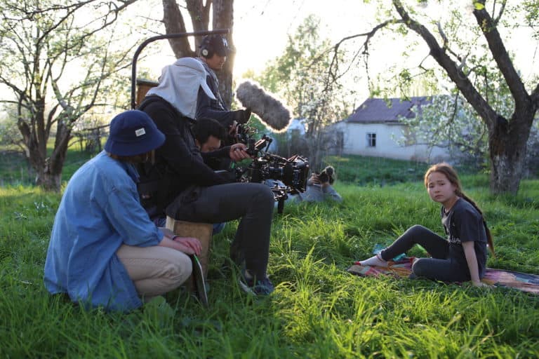 A man films a girl sitting on the grass under a tree