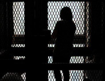 Silhouette of a woman behind a metal fence.
