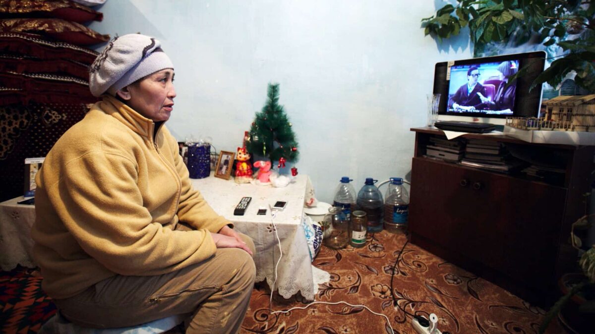 A woman sits in a living room watching television.