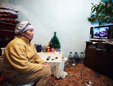 A woman sits in a living room watching television.