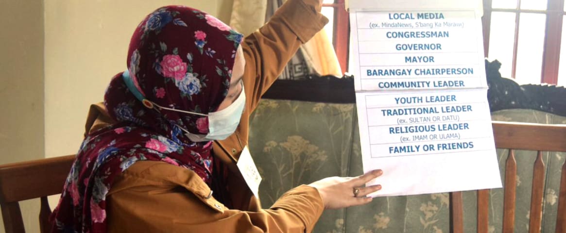 A woman holds up a list of community groups involved in rumor tracking.