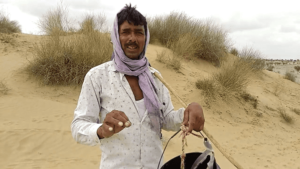 A man stands in a desert holding a pail.