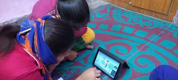 Two girls sit on the floor working on a tablet.