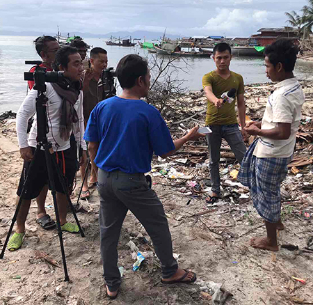 A group of people stand in a circle on a beach - one person is filming