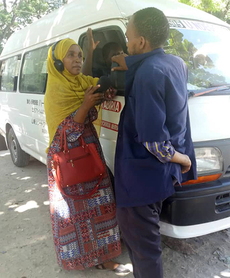 A woman wearing headphones and holding a mic interviews a man while they are standing next to a van