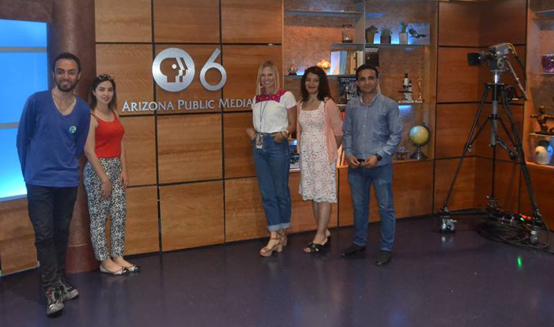 Two men and three women pose beside a sign that says, "Arizona Public Media"