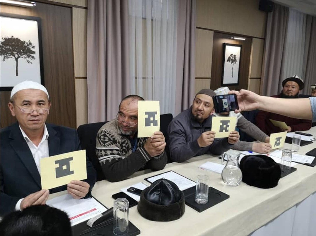 Five men sit behind a table holding up cards with symbols on them