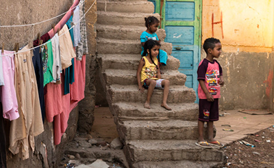 3 children on concrete steps, 2 sitting, 1 standing; clothes hang on a clothesline nearby