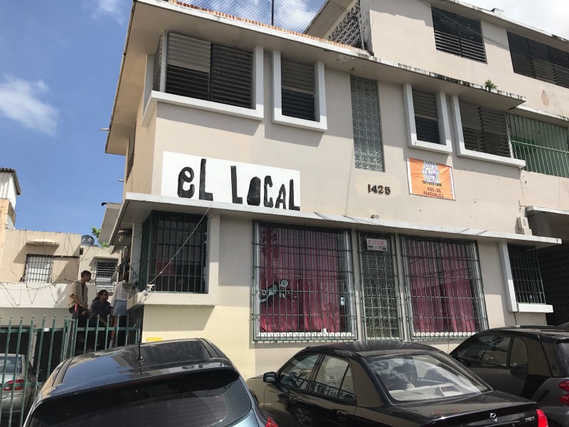 A 3 story stucco building with the sign "El Local" on it.