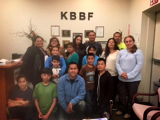 A group of people pose in front of a KBBF sign