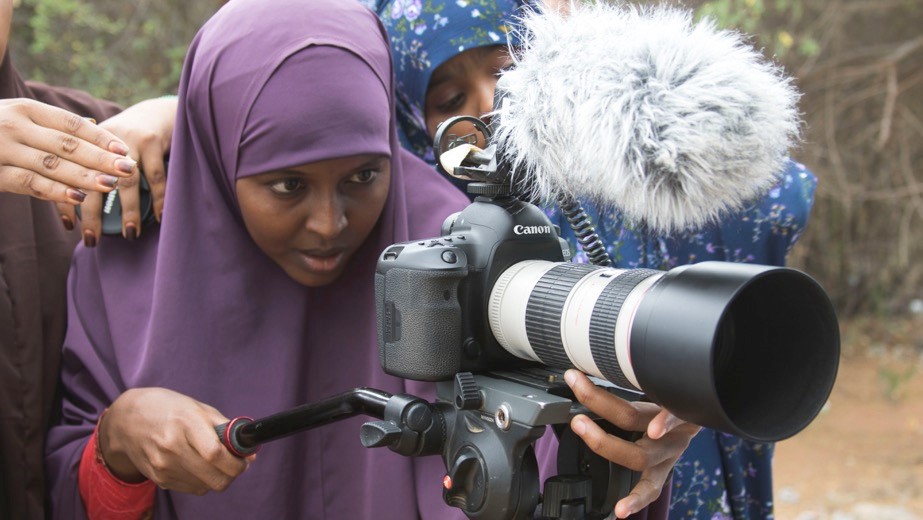 A young woman looks through the lens of a video camera