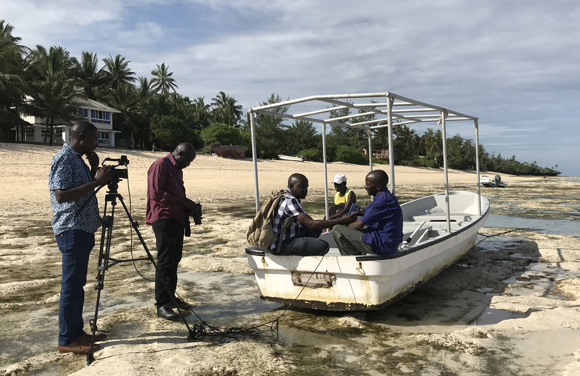 Two men stand interviewing 2 people sitting in a boat