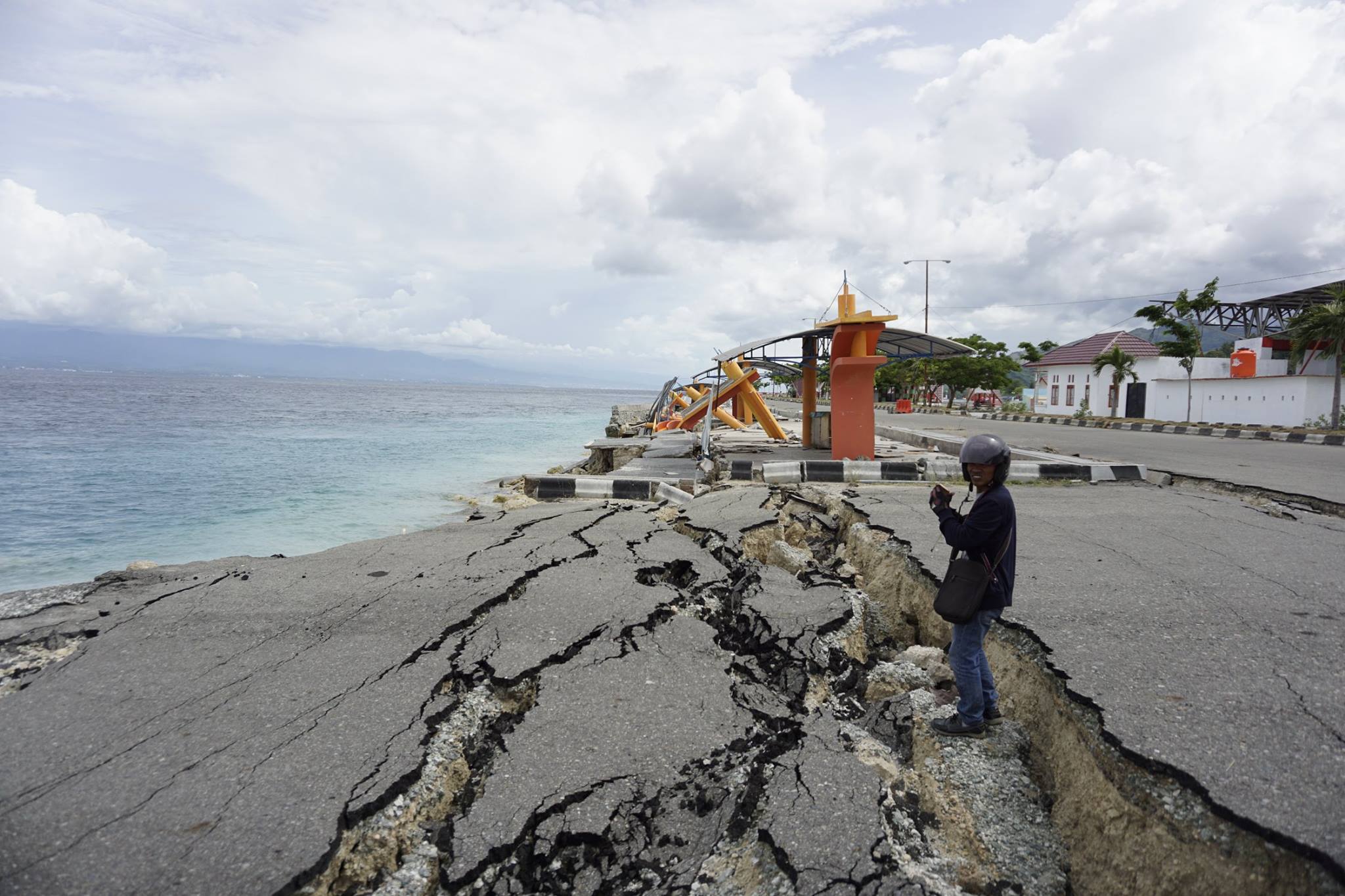 A man stands at the edge of the ocean on a road damaged by the tsunami.