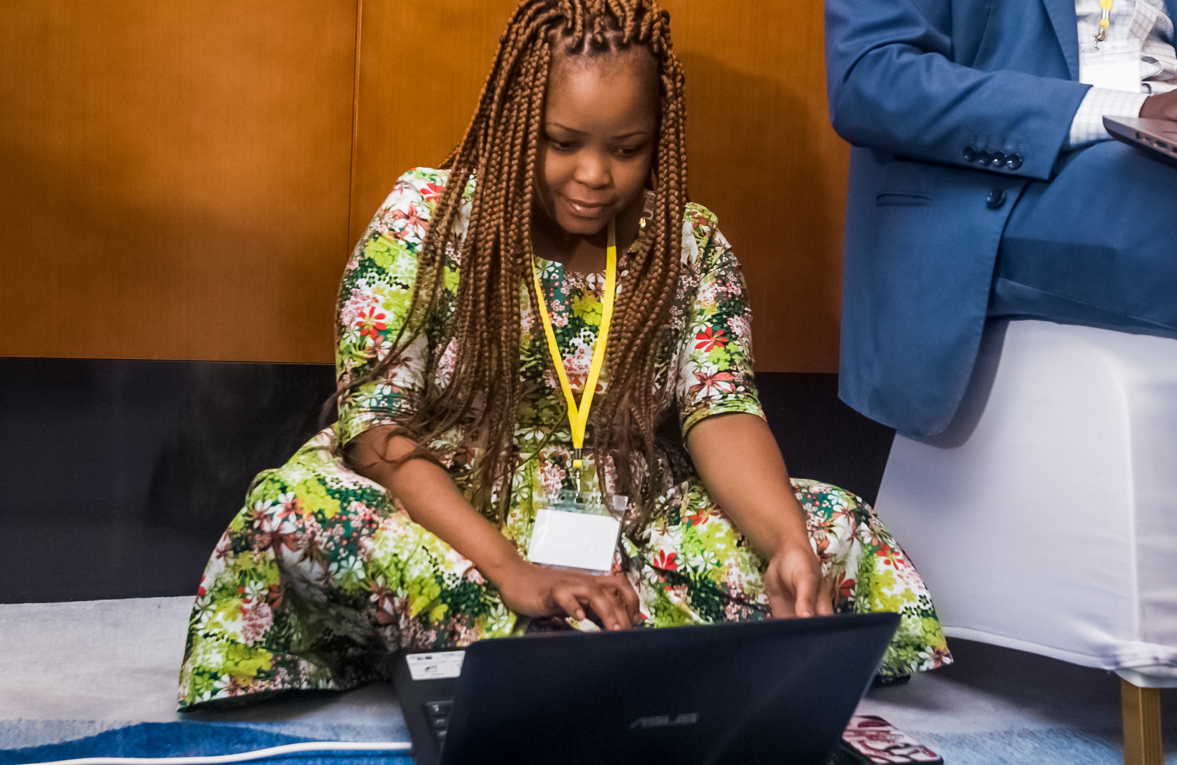 A woman sits on the floor working on a laptop computer.