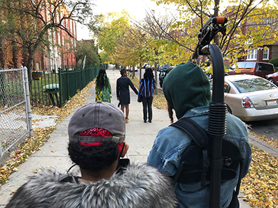 The backs of two people in the foreground who are filming 3 girls in the background