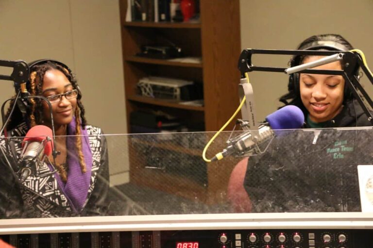 Two women sit at mics in a radio studio.
