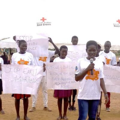 A group of girls stand holding posters that say "Stop early marriage"