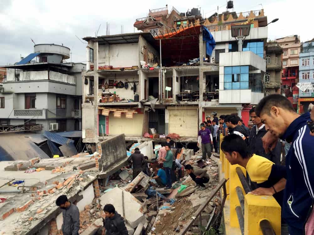 People stand looking at an earthquake-damaged building.
