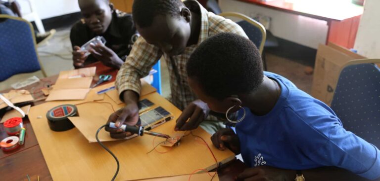Three young people work on a computer board with a soldering iron.