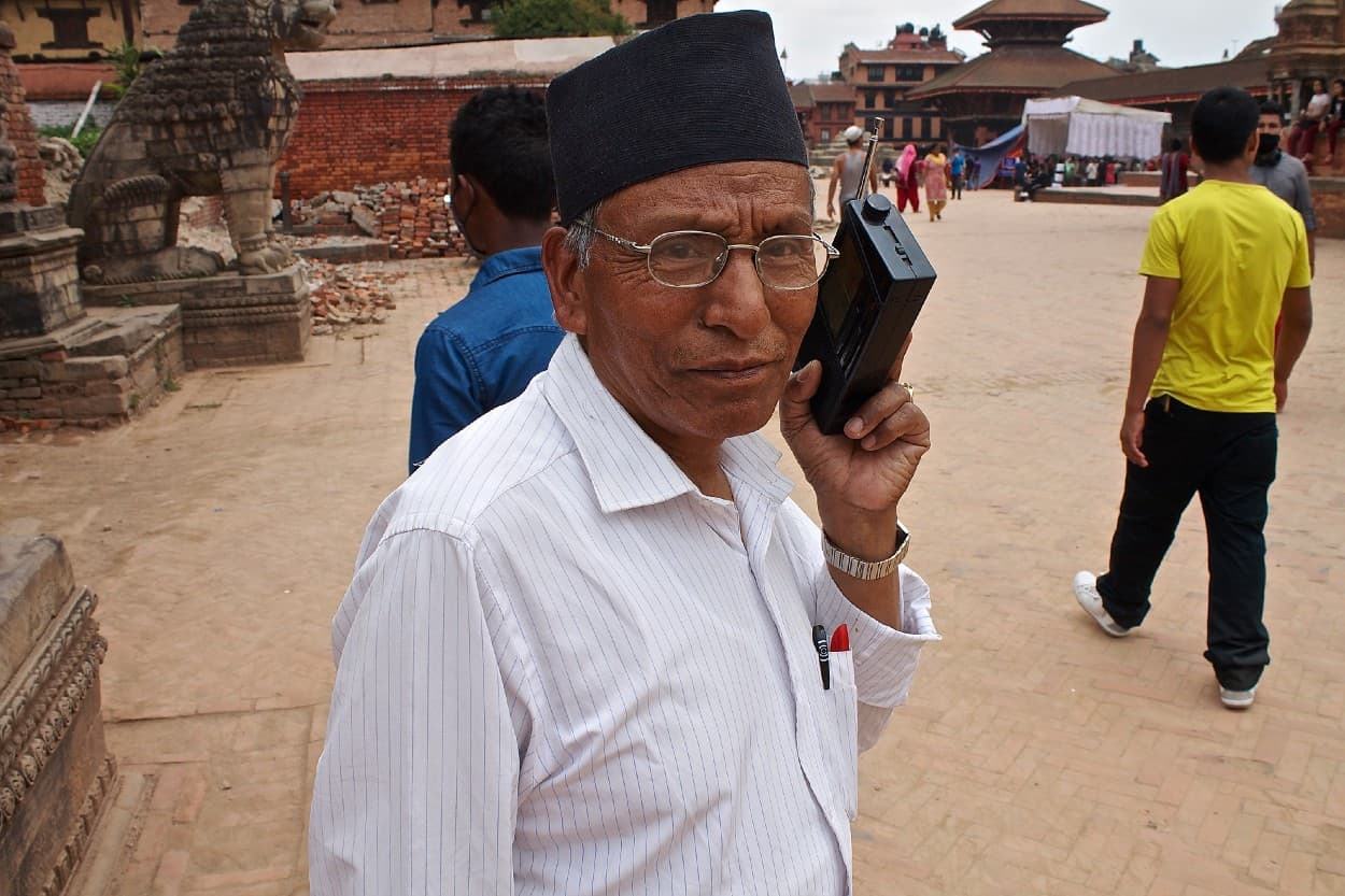 A man stands outside holding a portable radio to his ear.
