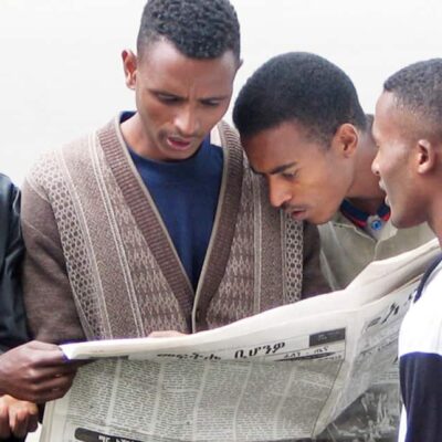 Four men stand together reading a newspaper.