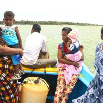 A man and three women on a small boat; two women are holding children.