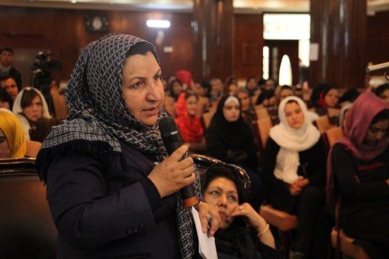 In a crowded room, a woman speaks into a mic.