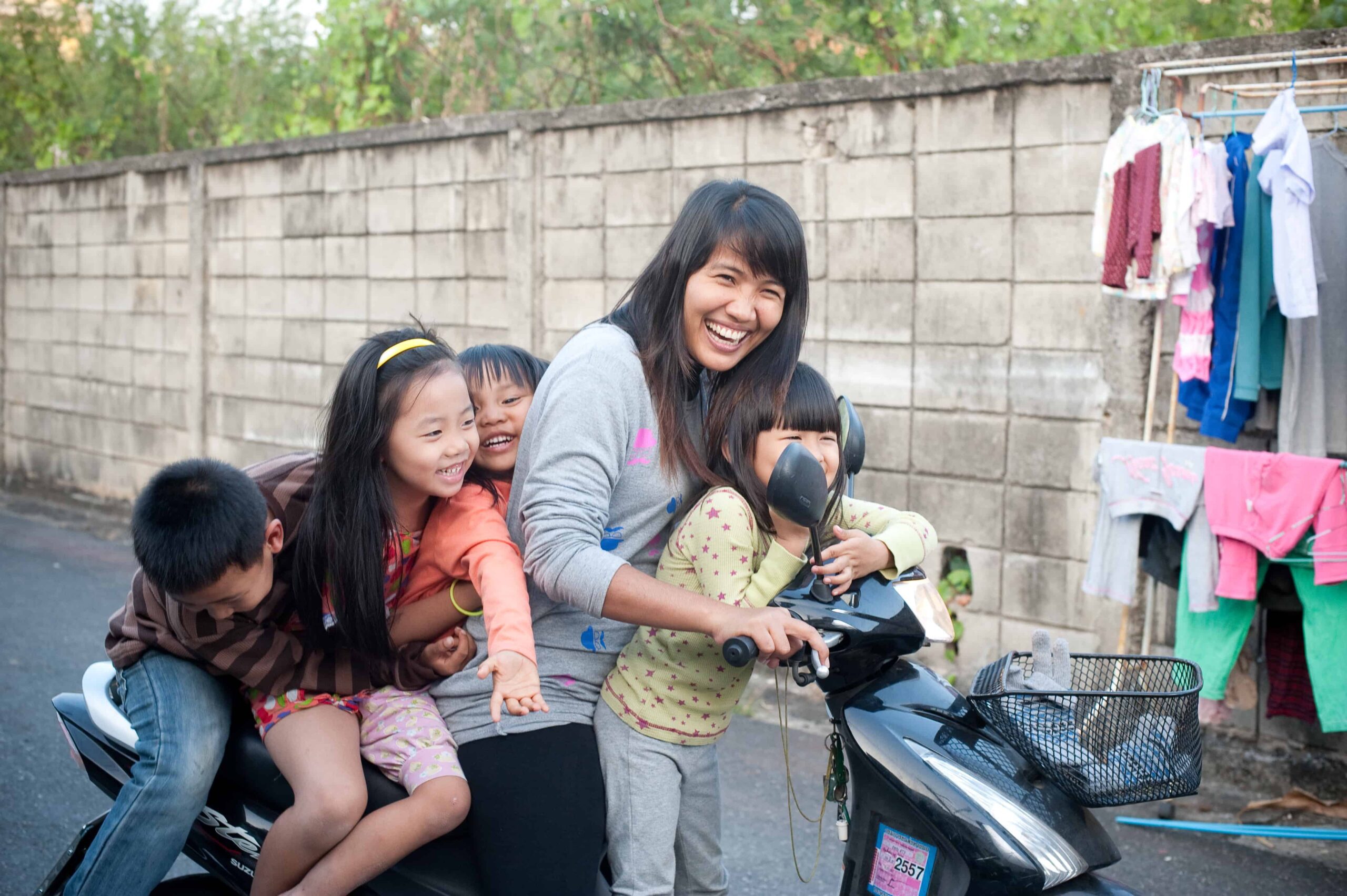 A woman on her motorbike with four children. They are laughing.
