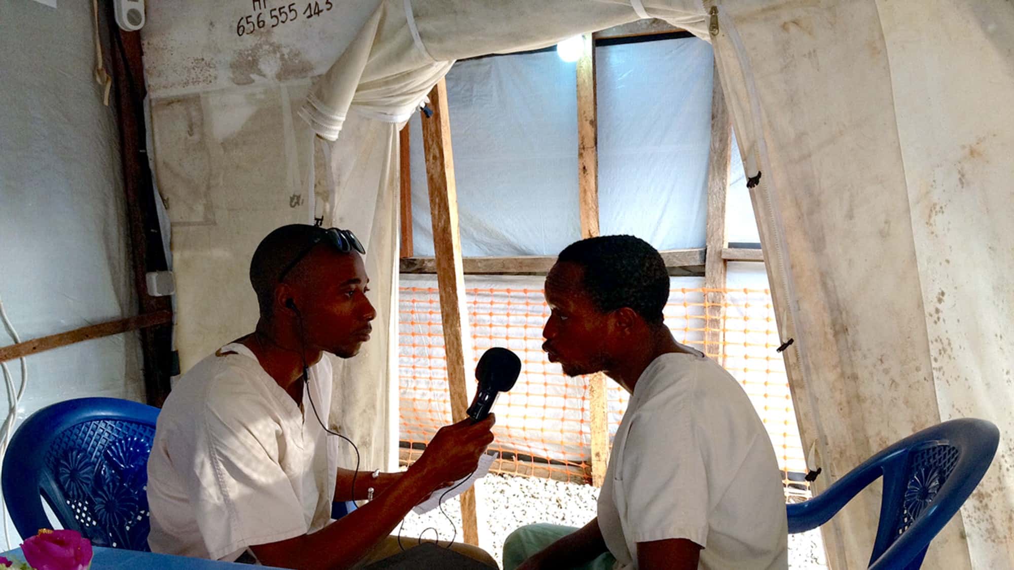A man interviews another man in a tent.