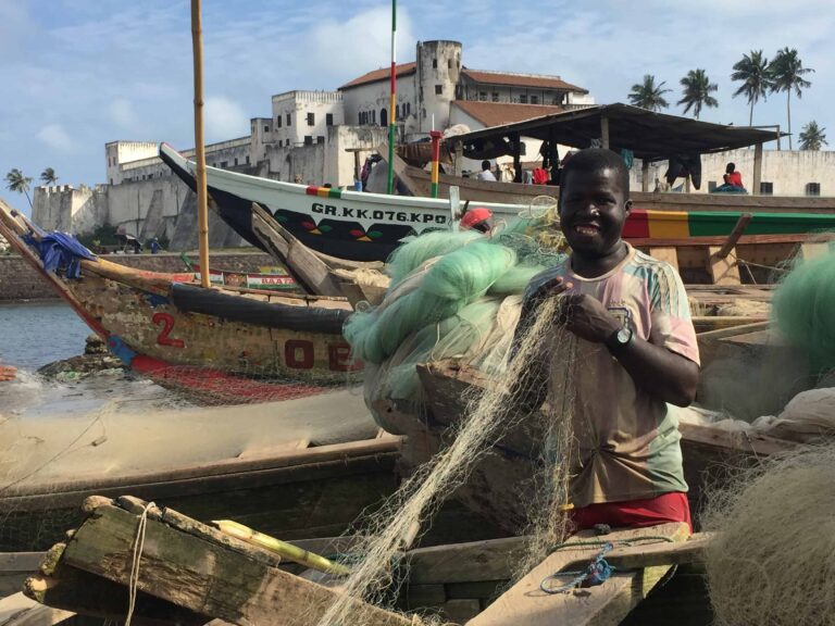 A man holds a fishing net by a boat.