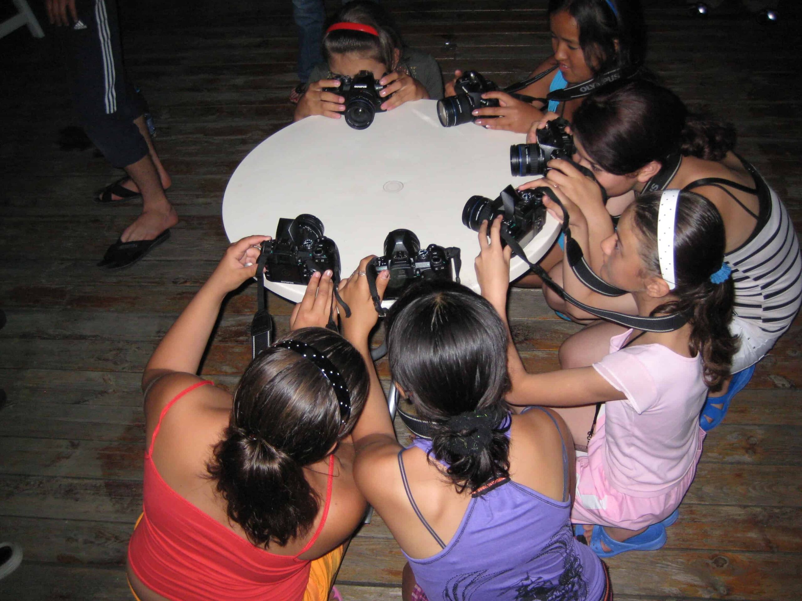 Young women around a table photograph each other.