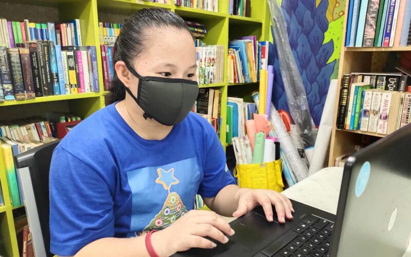 A young woman wearing a face mask sits typing at a computer