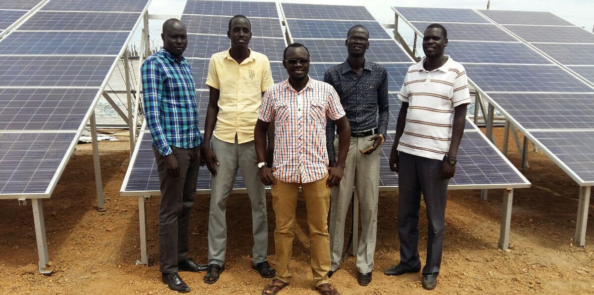 Five men stand in front of a bank of solar panels.