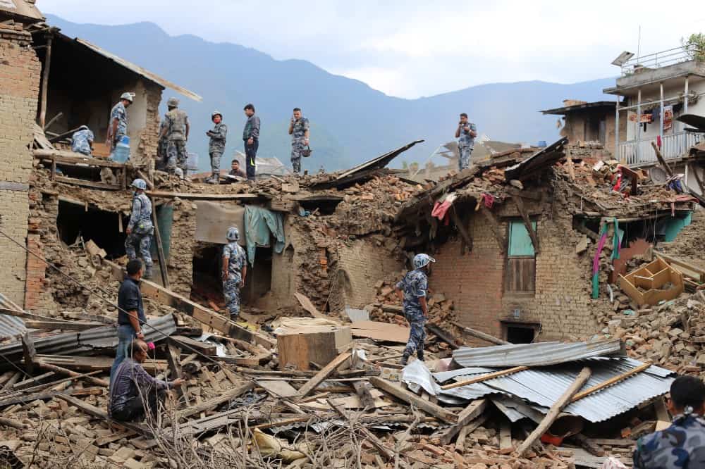 People in military gear look through the rubble of an earthquake-damaged building.