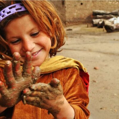 A little girl smears mud on her hands.