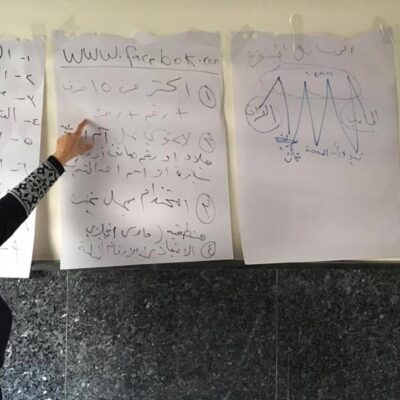 A woman points to writing on a large piece of paper mounted on a wall.