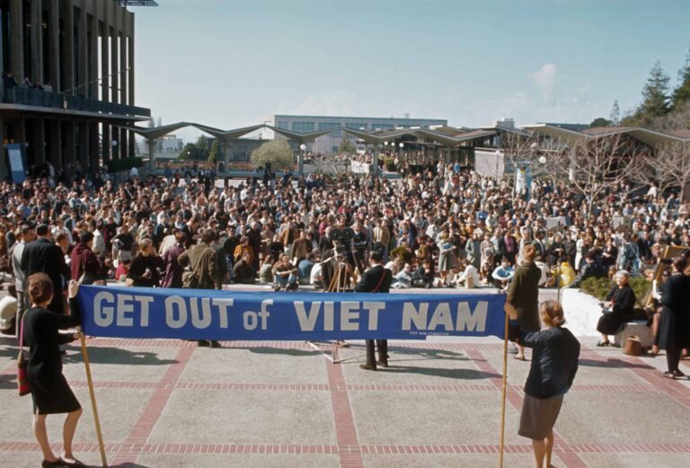 Two people hold a banner saying "Get out of Vietnam" at a protest.