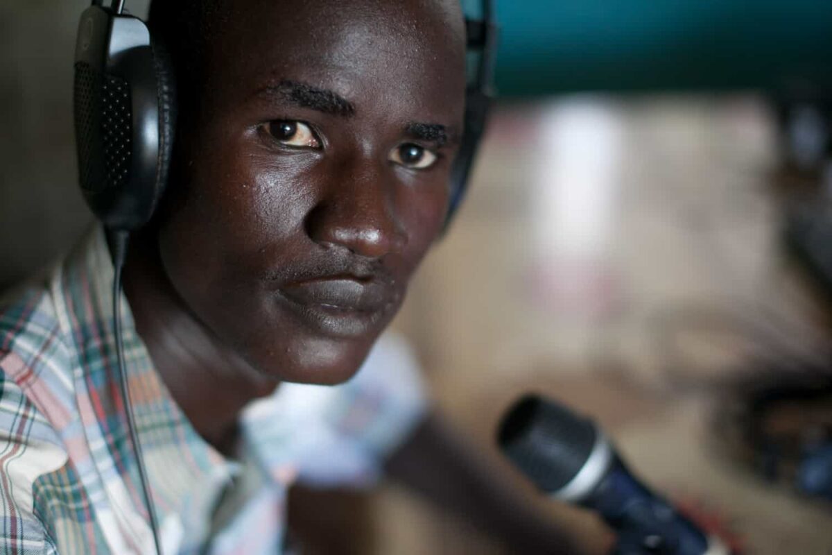 A man wears head phones and sits in front of a mic