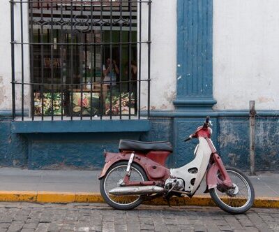 A motorbike is parked by the curb on a cobblestone street.