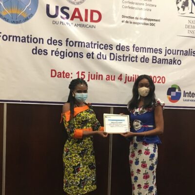 Two women wearing face masks stand on a stage, holding a certificate.
